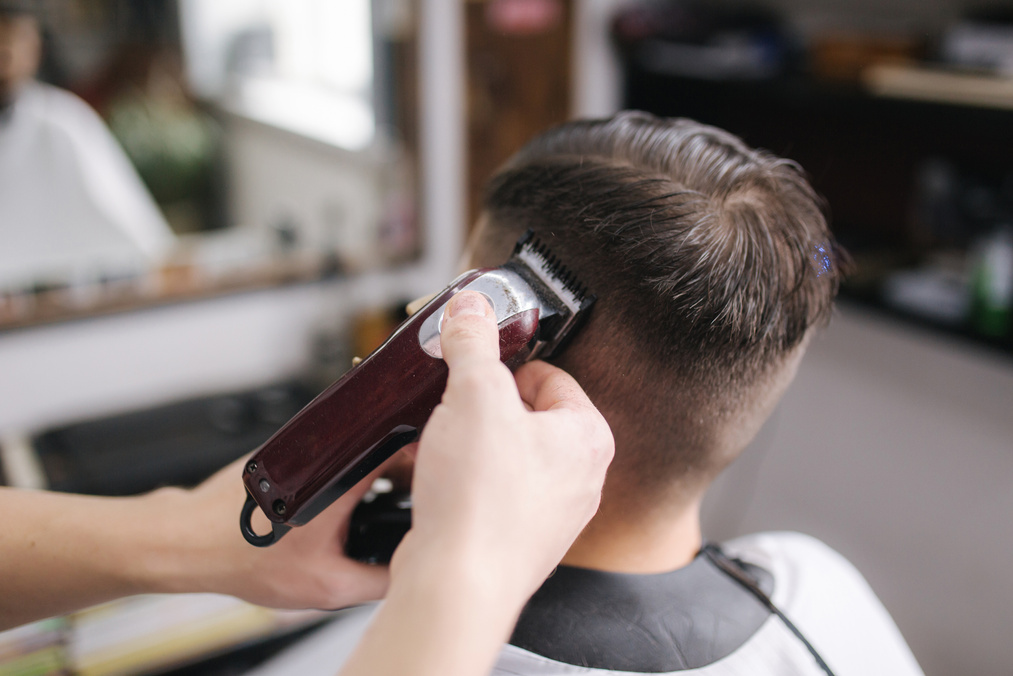 Back view of Men in beauty salon. Men's haircut in a barbershop. New haircut style 2021. Professional hairdresser uses a hair clipper for fringing hair